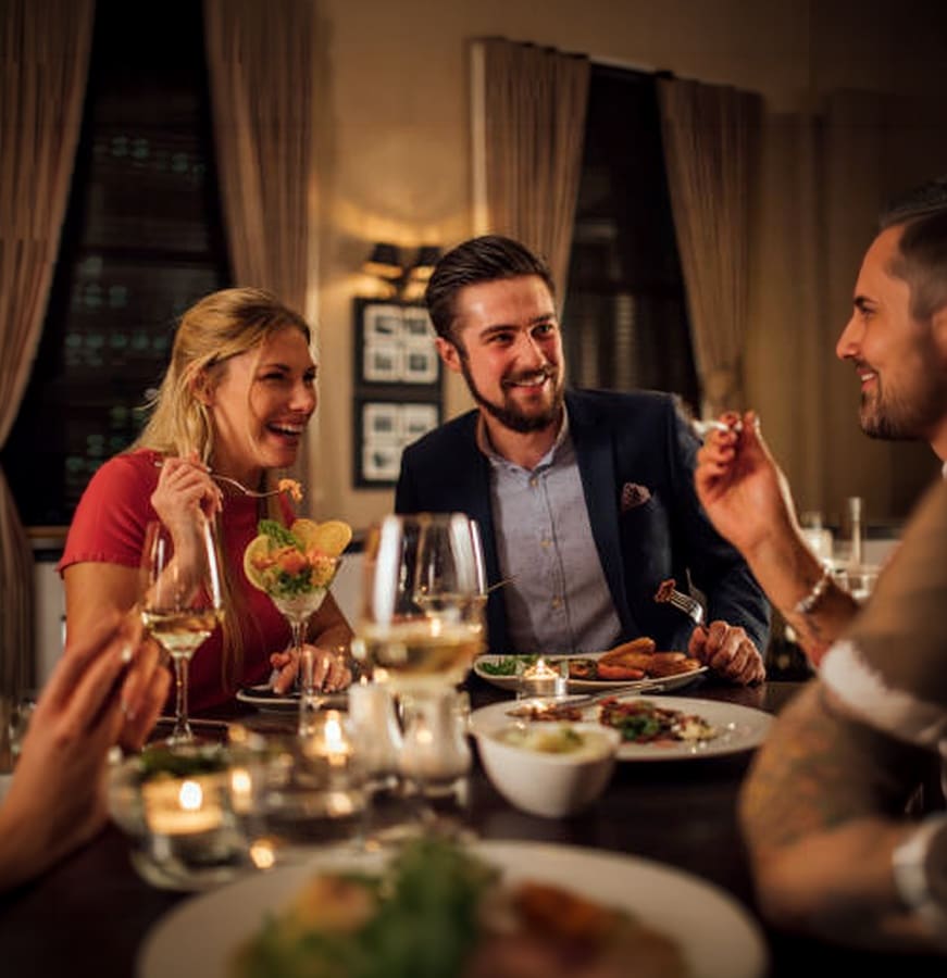 Two couples laughing over dinner and wine at a candlelit restaurant